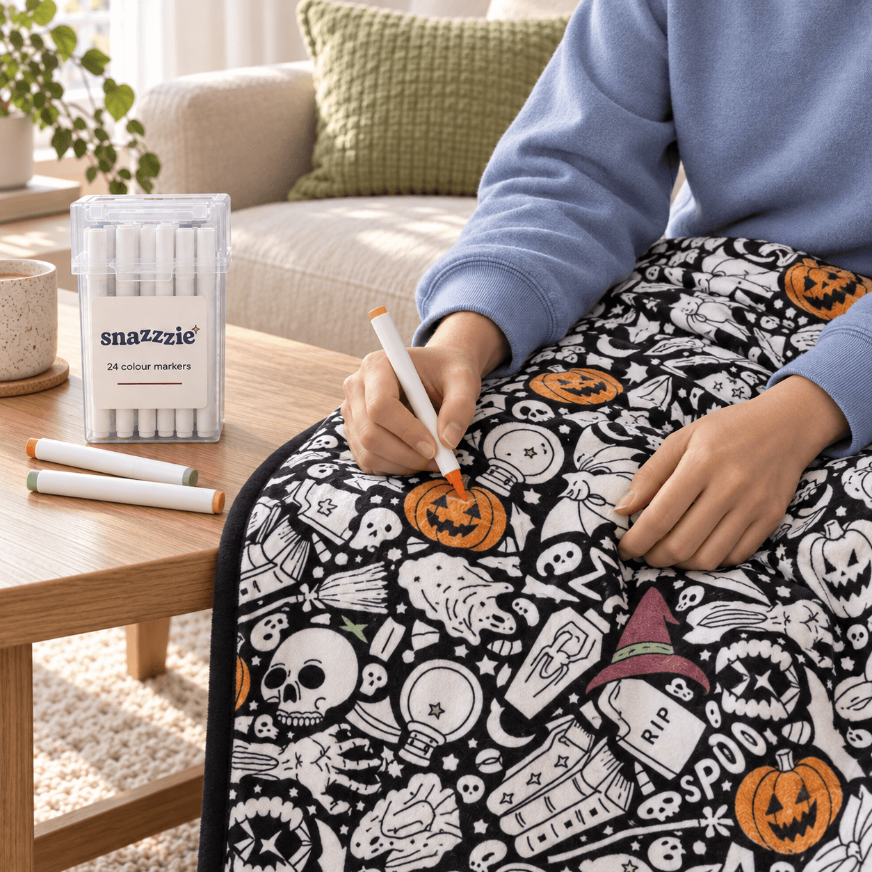 Hands adding colour to the Spooky Season Halloween coloring blanket with its marker case nearby