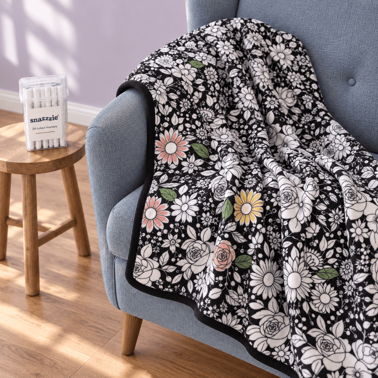 Partly coloured Flower Power blanket draped over a blue armchair, with its marker case on a wooden stool